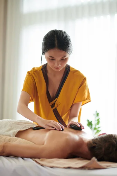 Young Masseuse Putting Hot Basalt Stones Spine Woman — Stock Photo, Image