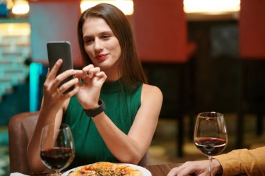 Smiling young woman taking selfie in fancy restaurant to post on social media