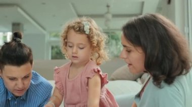 Evinde kağıt üzerinde resim çizerken pastel boya kullanan ve boş zamanlarını iki annesiyle geçiren beyaz bir kız.
