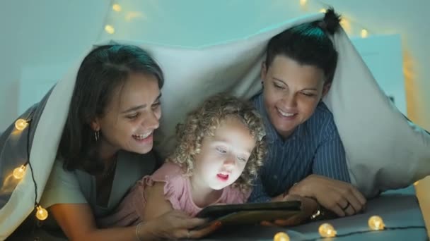 Szczęśliwa Para Lesbijek Ukochaną Córeczką Ogląda Filmy Tablecie Cyfrowym Leżącym — Wideo stockowe