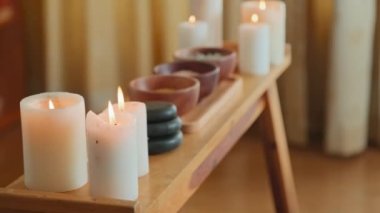 Wooden table with burning candles, massage stones and clay bowls in bright luxurious spa salon
