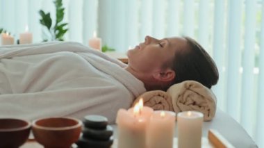 Relaxed young Caucasian woman lying with her eyes closed on massage bed in bright luxury spa salon