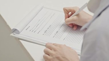 Close up shot of hands of female doctor filling out medical form at desk