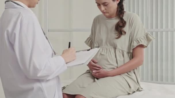 妊婦は医療用ソファに座って 診療所の女性医師との早産相談中に腹を撫でて — ストック動画