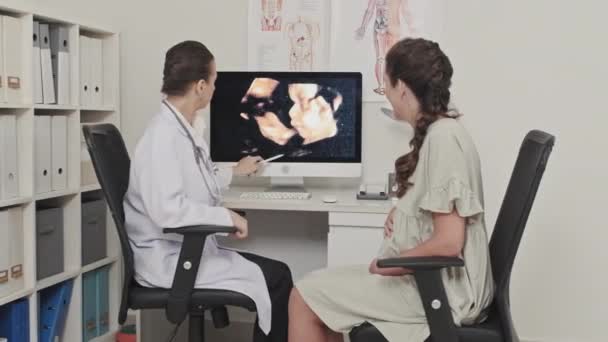 コンピューター画面に赤ちゃんの超音波検査を表示し 診療所で出産前の相談時に妊婦に説明する女性医師 — ストック動画