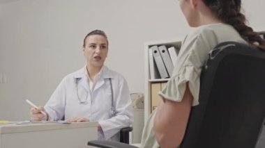 Kadın jinekolog, klinikte masa başında hamile bir kadınla doğum öncesi muayenesi yaparken konuşuyor.