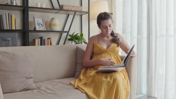 Ciężarna Kobieta Siedzi Kanapie Domu Głaska Się Brzuchu Czyta Książkę — Wideo stockowe