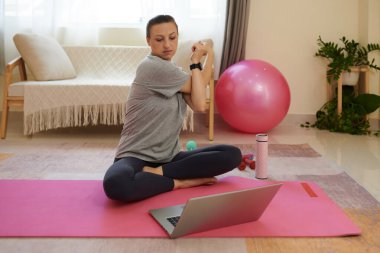 Woman stretching arms when warming up before training with online fitness instructor