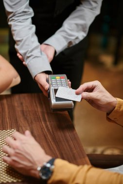 Hands of man paying for dinner in restaurant with contactless card