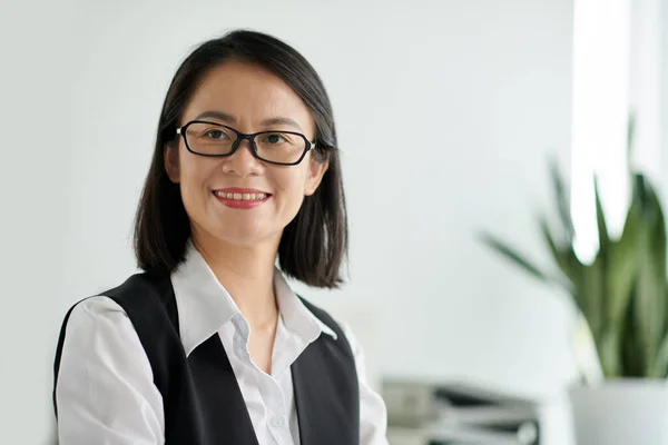 Portrait of smiling social worker in glasses standing in office and looking at camera
