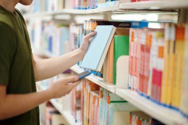 Cropped image of college student taking book from shelf in library