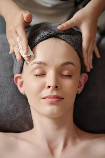 Esthetician wiping face of client with cotton pad soaked in toner