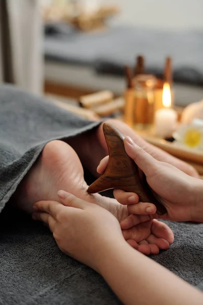 Feet of woman getting reflexology feet massage with wooden sticks