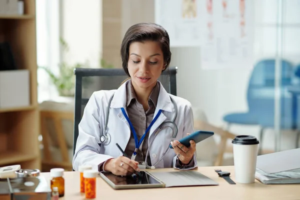 Pozytywny Szef Kliniki Medycznej Sprawdza Smartfona Robi Notatki Planerze — Zdjęcie stockowe