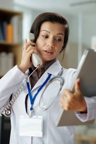 Portrait of physician checking medical history of patient when talking on phone with him