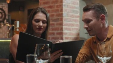Genç çift restoranda yemek yerken menüye bakıp birlikte yemek seçiyor.