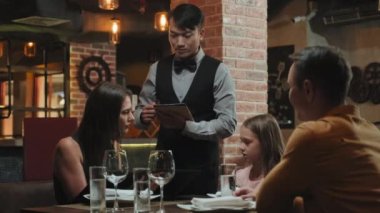 Restoranda dijital tabletle sipariş verirken Asyalı garsonla konuşan aile.