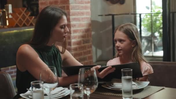 レストランのテーブルに座っている間 母親と小さな娘の中ショットは メニューで料理を選択し 議論します — ストック動画
