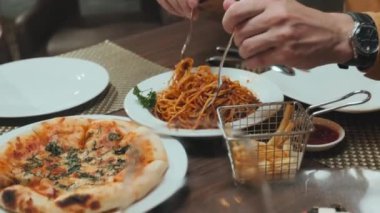 Spagetti sosu karıştıran ve restoranda yemek yerken pizza kesen çiftin yakın plan çekimleri.