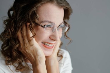 Yüzüne dokunan gözlüklü neşeli orta yaşlı kadın portresi.
