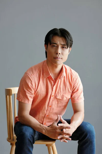 灰色の壁に対して椅子に座っている若いアジア人男性を自信を持って — ストック写真