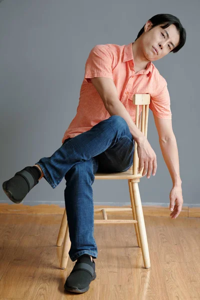 若いです男でジーンズとサーモンシャツ座っています上の椅子 — ストック写真