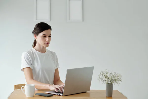 穿着白色T恤衫的年轻妇女在办公桌旁的笔记本电脑上工作 — 图库照片