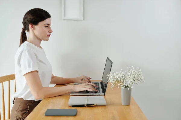 Serious young woman working on laptop at desk in her home office