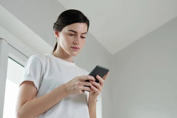 Serious young woman reading notification on smartphone
