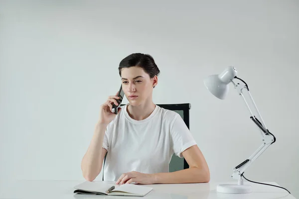 若い女性はオフィスの机に座って電話で話しています — ストック写真
