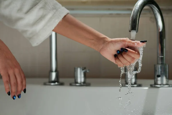 Hand of woman touching tap water when filling bathtub