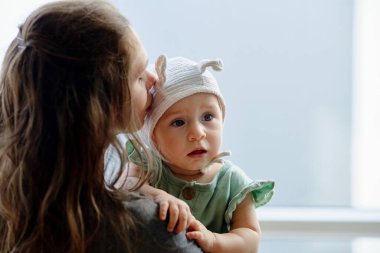 Anne, sevimli, meraklı küçük kızını başından öpüyor.