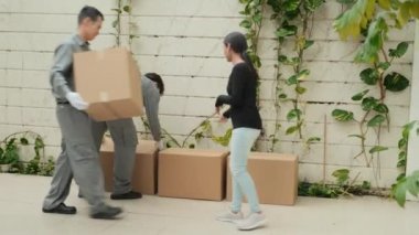 Asyalı ev sahipleri talimat verirken, servis elemanlarının evin önüne karton kutular ve kanepe getirmesi.