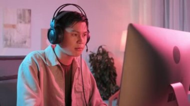 Evde oynadığı bilgisayar oyununda mikrofonlu Asyalı gencin orta boy görüntüsü.