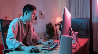 Asyalı gen z oyuncusunun beli neon pembe ışıklandırmalı heyecan verici online bilgisayar oyunu oynuyor.