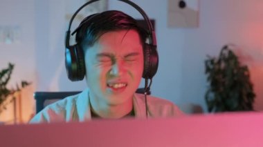 Heyecanlı Asyalı oyuncu geceleri çevrimiçi bilgisayar oyunu oynarken kulaklığına mikrofonla konuşuyor.