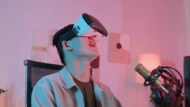 VR kulaklıklı heyecanlı Asyalı adam gecenin geç saatlerinde evde oyun oynuyor. Karanlık odada bilgisayar başında, neon pembe ışıklı.