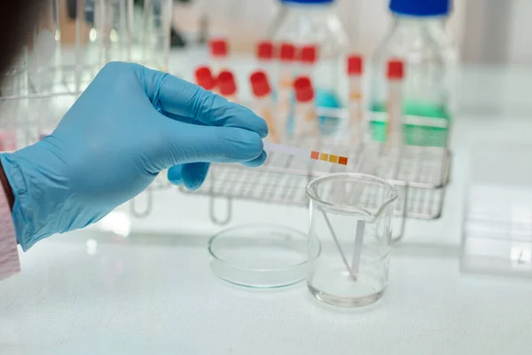 实验室工作时 化学人员在玻璃器皿上握着Ph酸指示剂的手套手 — 图库照片