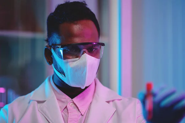 臨床研究中の新しいワクチンや薬のサンプルを見て保護マスクや眼鏡中の若い深刻な男性化学者 — ストック写真