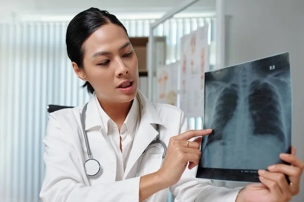 ラボコートの若い女性放射線科医は 医療室に座っている間 オンライン相談中に患者に肺のX線をコメント — ストック写真