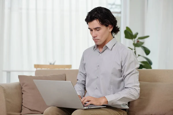 Jonge Mannelijke Analist Typen Laptop Toetsenbord Terwijl Zitten Bank Huis — Stockfoto
