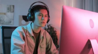 Karanlık odada neon ışıkla bilgisayar oyunu oynarken hayal kırıklığına uğrayan Asyalı genç oyuncunun belini kaldırın.