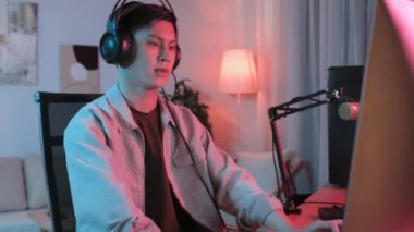 Asyalı çocuğun karanlık bir odada bilgisayar başında neon ışıklandırmayla video oyunu oynarken orta boy görüntüsü.