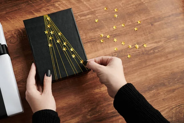 Руки Женщины Приклеивающей Сверкающие Звезды Подарочной Коробке Завернутой Черную Бумагу — стоковое фото