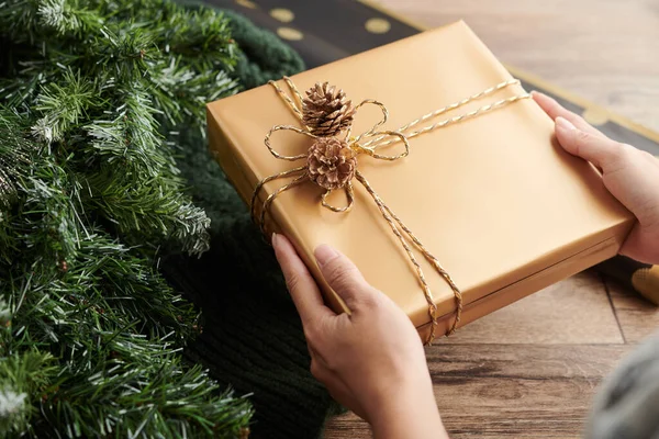 Руки Рождественским Подарком Завернутые Золотую Бумагу Украшенные Сосновыми Шишками — стоковое фото