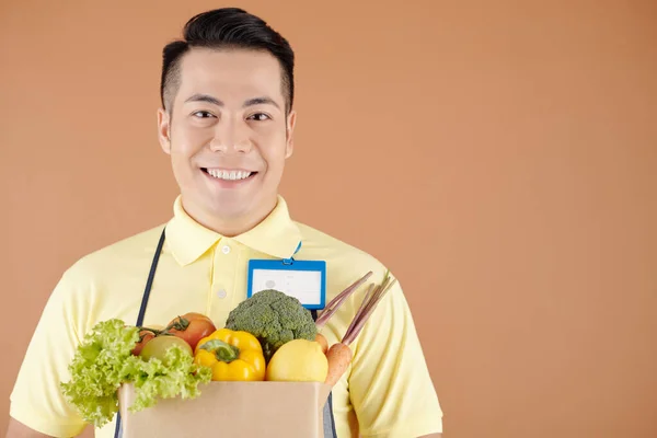 新鮮な野菜の紙袋を持つ陽気な配達サービスや暗い店の労働者の肖像画 — ストック写真