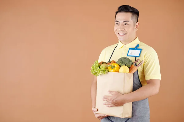 Szczęśliwy Azjatycki Pracownik Ciemnego Sklepu Przewożący Torbę Świeżych Produktów Zebranych — Zdjęcie stockowe
