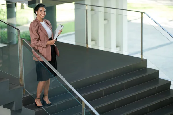 正の若い女性起業家がオフィスでステップに立って手にクリップボードを保持 — ストック写真