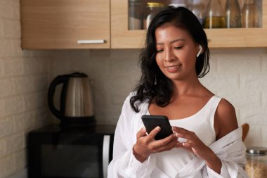 Video görüşmesi yaparken ya da akıllı telefondan müzik dinlerken kulaklık takan gülümseyen genç bir kadın.