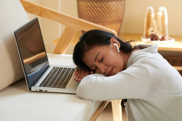 睡眠不足的女学生 耳边带着耳塞靠着桌子 打开笔记本电脑 — 图库照片